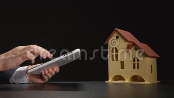 商人手中拿着一台平板电脑靠近桌子上的房子模型靠近视频的预览图