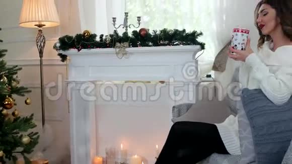 女孩在靠近壁炉和圣诞树的客厅里喝杯茶在家过寒假很惬意视频的预览图