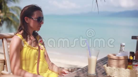 年轻女子戴着墨镜夏天喝着鸡尾酒在海边的海滩咖啡馆里尽情享受假期视频的预览图