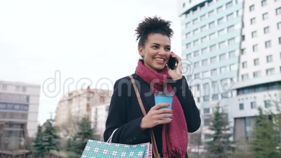 漂亮的混血商务女性会说智能手机还会拿着购物袋在城市大街上喝咖啡视频的预览图