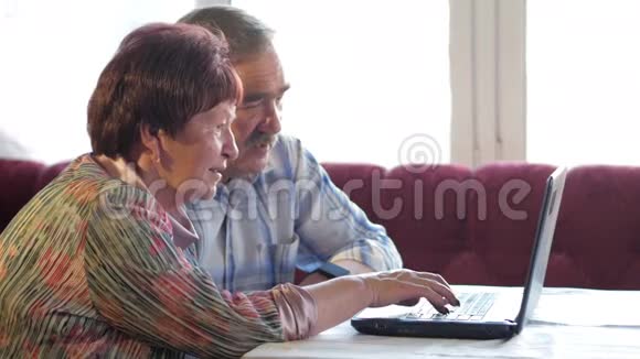 一对老夫妇坐在家里的笔记本电脑上一个女人看新闻一个留着胡子的男人坐在他旁边说话视频的预览图