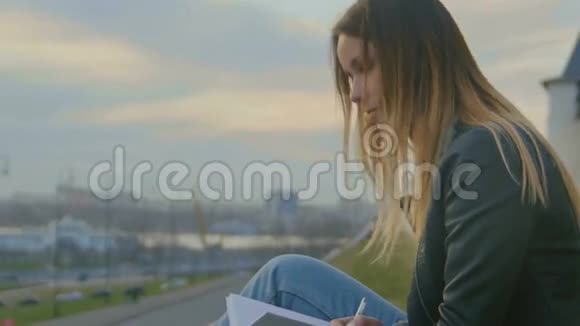 可爱的小女孩写日记坐在城市景色的背景下黄昏时关门视频的预览图