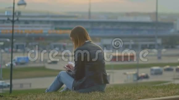 可爱的小女孩写日记坐在城市景色的背景下黄昏狭窄视频的预览图
