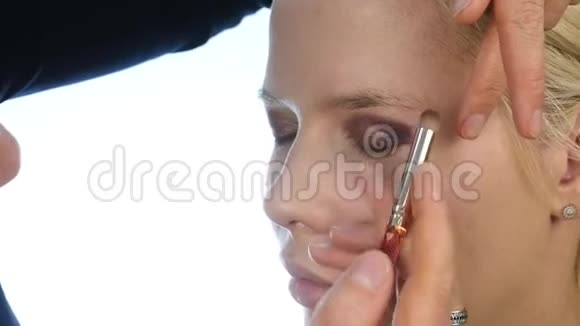 女性造型师用特殊的画笔在金发新娘的眼皮上涂上深色的眼影婚礼化妆慢动作视频的预览图
