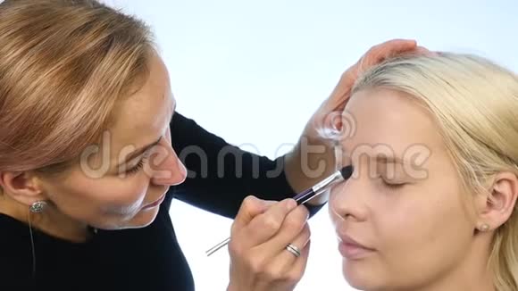 女性造型师用特殊的画笔在金发新娘的眼皮上涂上深色的眼影婚礼化妆慢动作视频的预览图
