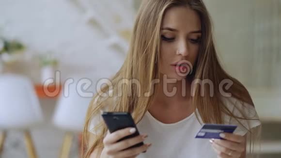 美丽的年轻女性在家使用智能手机和信用卡进行网上银行和购物视频的预览图