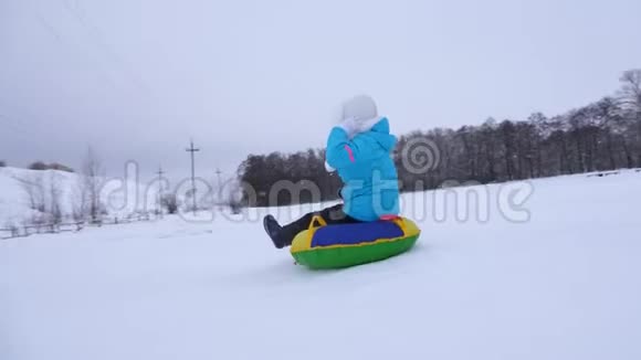 年轻的女孩滑下雪滑在一个充气雪管和波浪她的手快乐女孩在公园里玩视频的预览图