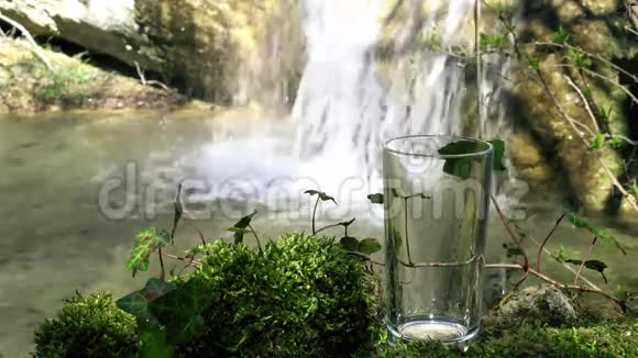 玻璃饮用天然水与瀑布在柔和的焦点背景从泉水中流出的纯净生态水视频的预览图