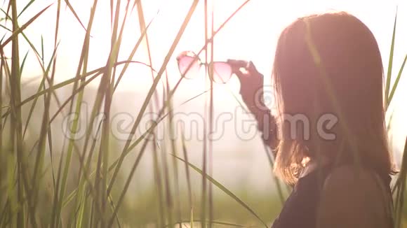 穿着黑色衣服的年轻女子戴上太阳眼镜日落视频的预览图