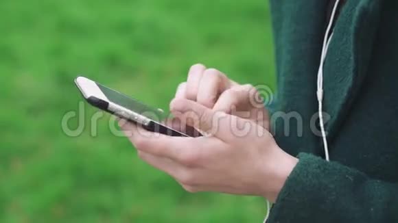 在草地背景4k上用带有耳机的手机关闭女性双手视频的预览图