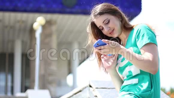 年轻漂亮的女人在公园长椅上玩她的触摸电话游戏视频的预览图