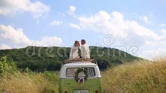 在阳光明媚的夏日里新婚快乐的新婚夫妇新娘和新郎坐在雷托婚礼巴士的顶端温柔的爱时刻视频的预览图