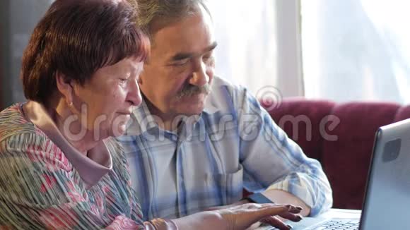 一对老夫妇坐在家里的笔记本电脑上一个女人看新闻一个留着胡子的男人坐在他旁边说话视频的预览图