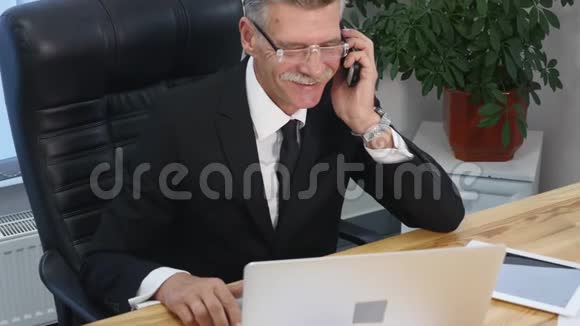 有着白色智能手机的老人在办公室说话微笑视频的预览图