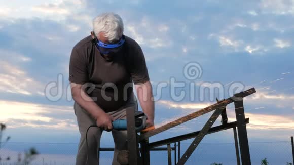 一个年纪大的人在日落时切断了一个金属角磨床工人后面美丽的天空视频的预览图