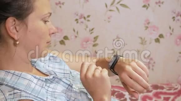 年轻女子在家里的沙发上查看智能手表上的信息视频的预览图