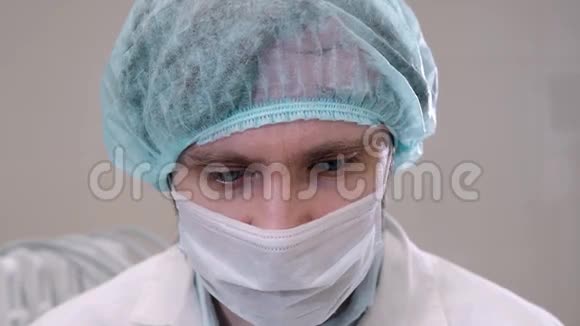 戴着面具的英俊外科医生正看着摄像机站在一个现代化的手术室里紧闭着病人在诊所里视频的预览图