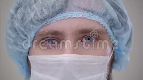 戴着面具的英俊外科医生正看着摄像机站在一个现代化的手术室里紧闭着病人在诊所里视频的预览图