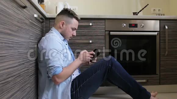 坐在厨房里玩平板电脑游戏的年轻人视频的预览图