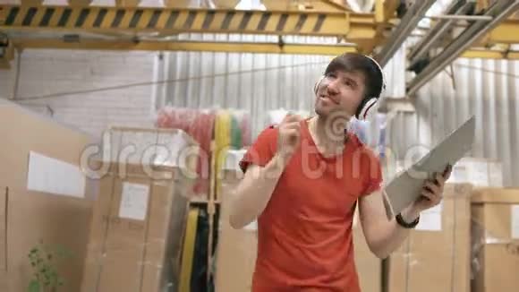 在工业仓库里听音乐和跳舞的快乐年轻工人的多利镜头戴耳机的人视频的预览图