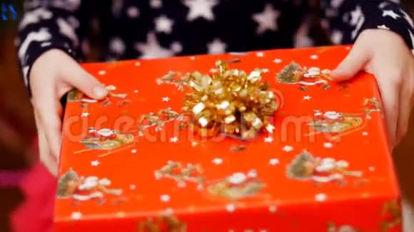 用一个金色的蝴蝶结用一个漂亮的彩色纸包装着一个圣诞礼物两只孩子的手紧紧地握着视频的预览图