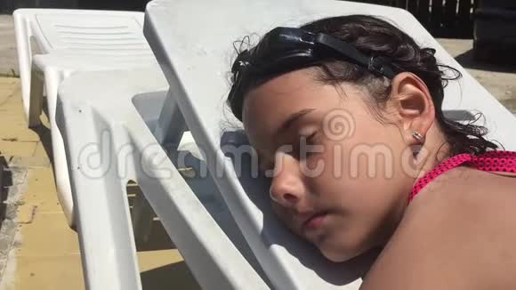 美丽的年轻女孩穿着泳衣躺在游泳池附近的躺椅上睡觉视频的预览图