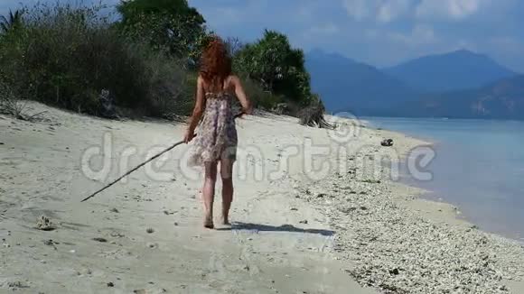 一个穿着夏装的女孩走在沙滩上用沙子画出形状视频的预览图