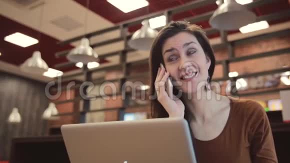 年轻的黑发女孩在笔记本电脑上工作在咖啡馆里打电话视频的预览图