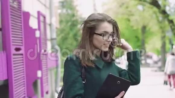 漂亮的女孩拿着平板电脑戴着眼镜在街头背景上微笑着视频的预览图