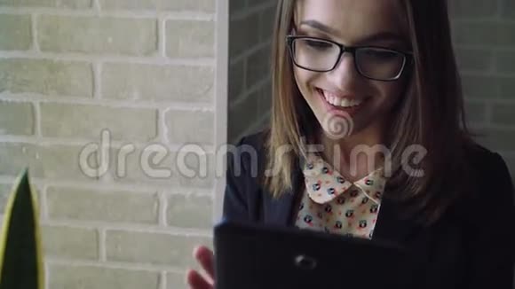 年轻的女人看着靠近窗户的平板电脑想知道4K视频的预览图