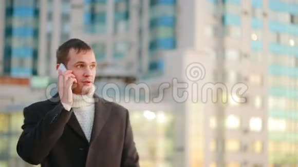 在摩天大楼背景下的现代城市里穿着外套带着手机的人视频的预览图