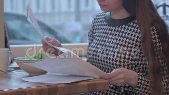 年轻女商人阅读文件的武器她正坐在咖啡馆的桌子旁吃着沙拉视频的预览图