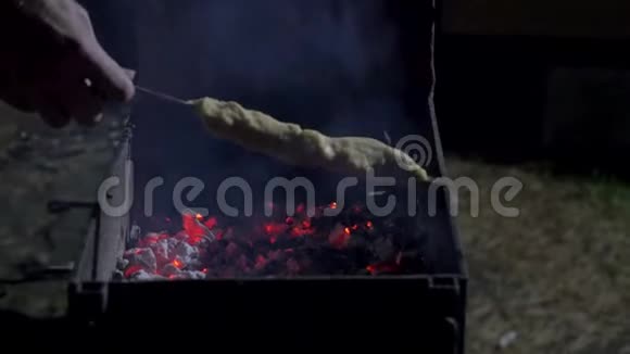 男人把生肉放在热烧烤架上用一对木钳烧烤在黑暗的背景下近距离观看视频的预览图