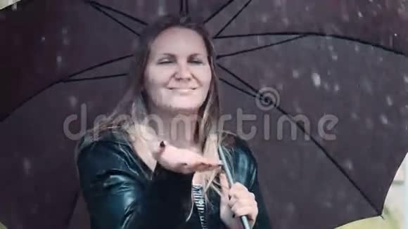 金发女人在黑色的扭转伞下享受雨视频的预览图