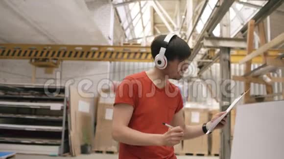 在工业仓库里听音乐和跳舞的快乐年轻工人的多利镜头戴耳机的人视频的预览图