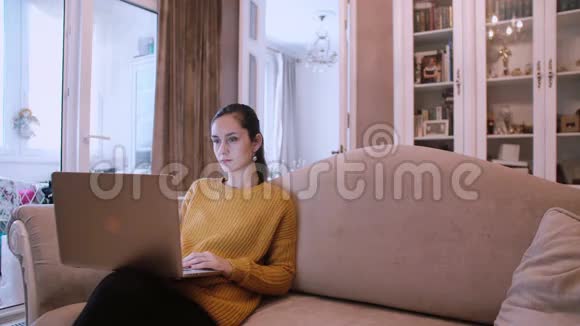 漂亮的女孩坐在沙发上在客厅的家里使用笔记本电脑视频的预览图