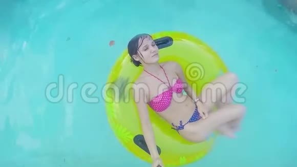 年轻女子在一个有黄色充气戒指的游泳池里放松最高看法视频的预览图
