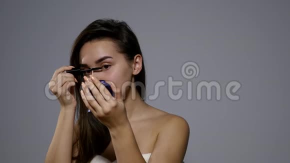 面部化妆年轻的深色女人用黑色睫毛膏为她的长睫毛画上一张特写镜头4K视频的预览图
