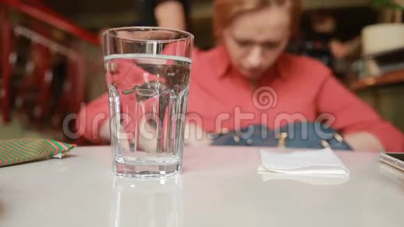 咖啡馆里的女孩正在寻找一个装有水的玻璃背景的袋子里的东西视频的预览图