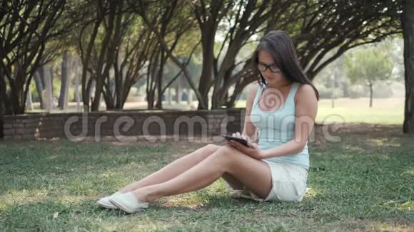 利用平板电脑网上购物理念年轻美丽的女孩坐在公园的草坪上视频的预览图