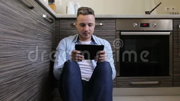 坐在厨房里玩平板电脑游戏的年轻人视频的预览图