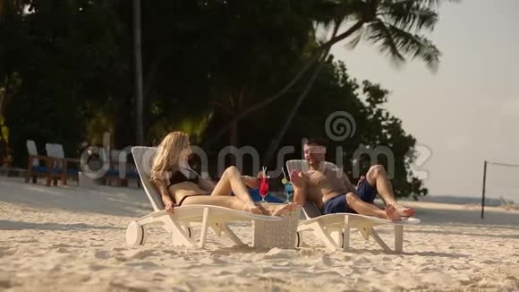 年轻的家庭夫妇在热带海滩晒日光浴和喝彩色鸡尾酒在异国度假的蜜月中情人视频的预览图