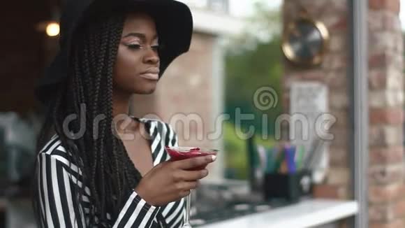 年轻优雅的非洲裔美国女人戴着黑色帽子在炎热的夏日喝鸡尾酒视频的预览图