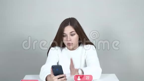 白种人女孩坐在桌子旁拿着智能手机对着镜头说话手势视频的预览图