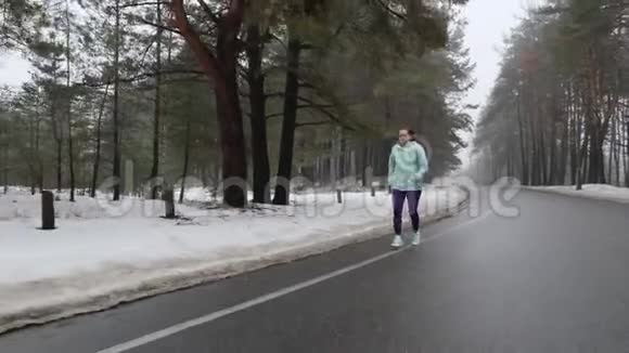 冬天一位高加索老太太戴着耳机在雪地公园里跑步前跟拍视频的预览图