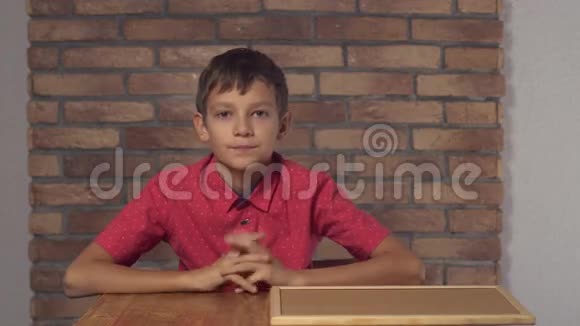坐在书桌前的孩子拿着一张写有字母的挂图你在背景红砖墙上怎么样视频的预览图