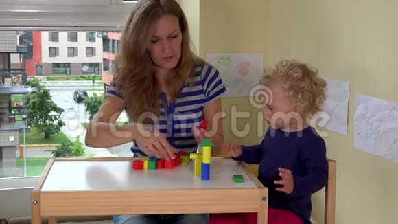 妈妈和她蹒跚学步的小女孩在小桌子上玩木砖玩具视频的预览图