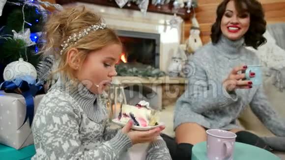 女孩在圣诞树上吃一大块蛋糕妈妈和女儿一家人在壁炉旁吃甜点视频的预览图