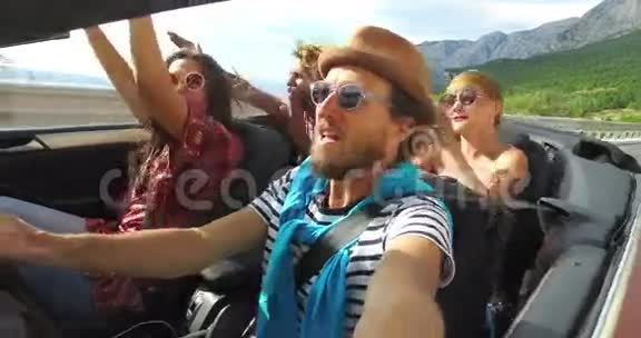 戴帽子的留胡子的时髦男人和朋友一起坐敞篷车听音乐视频的预览图