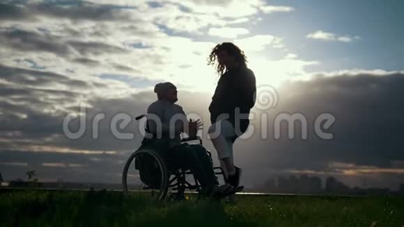 照顾残疾人坐轮椅的男人和女人在阴天日落时交谈视频的预览图
